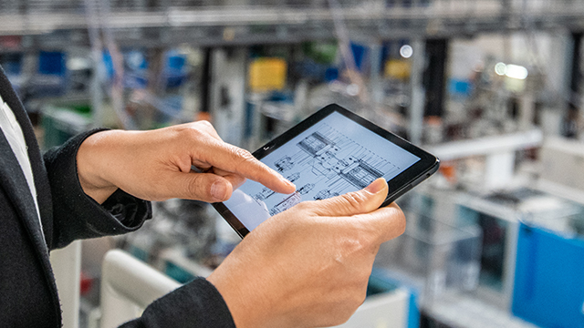 Hands holding and pointing to a tablet with a blueprint mapping design on it