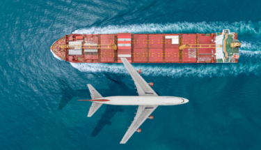 Passenger plane flying over the sea with cargo ship sailing on the sea